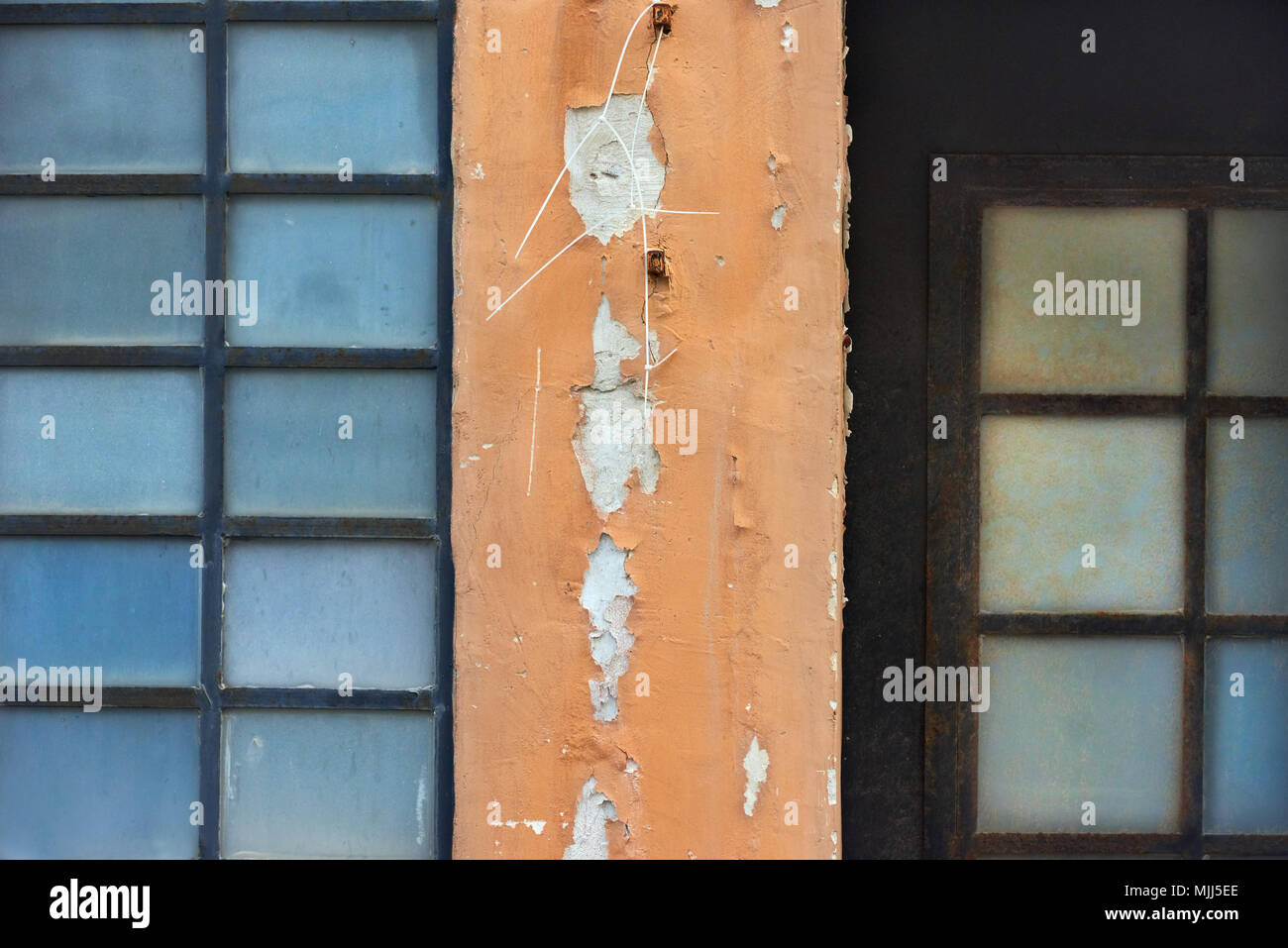 Alte Mauer mit Plätzen aus Metall - Kunststoff Fenster mit blauem Glas, in der Mitte ein Fragment der Wand mit orange Gips. Stockfoto