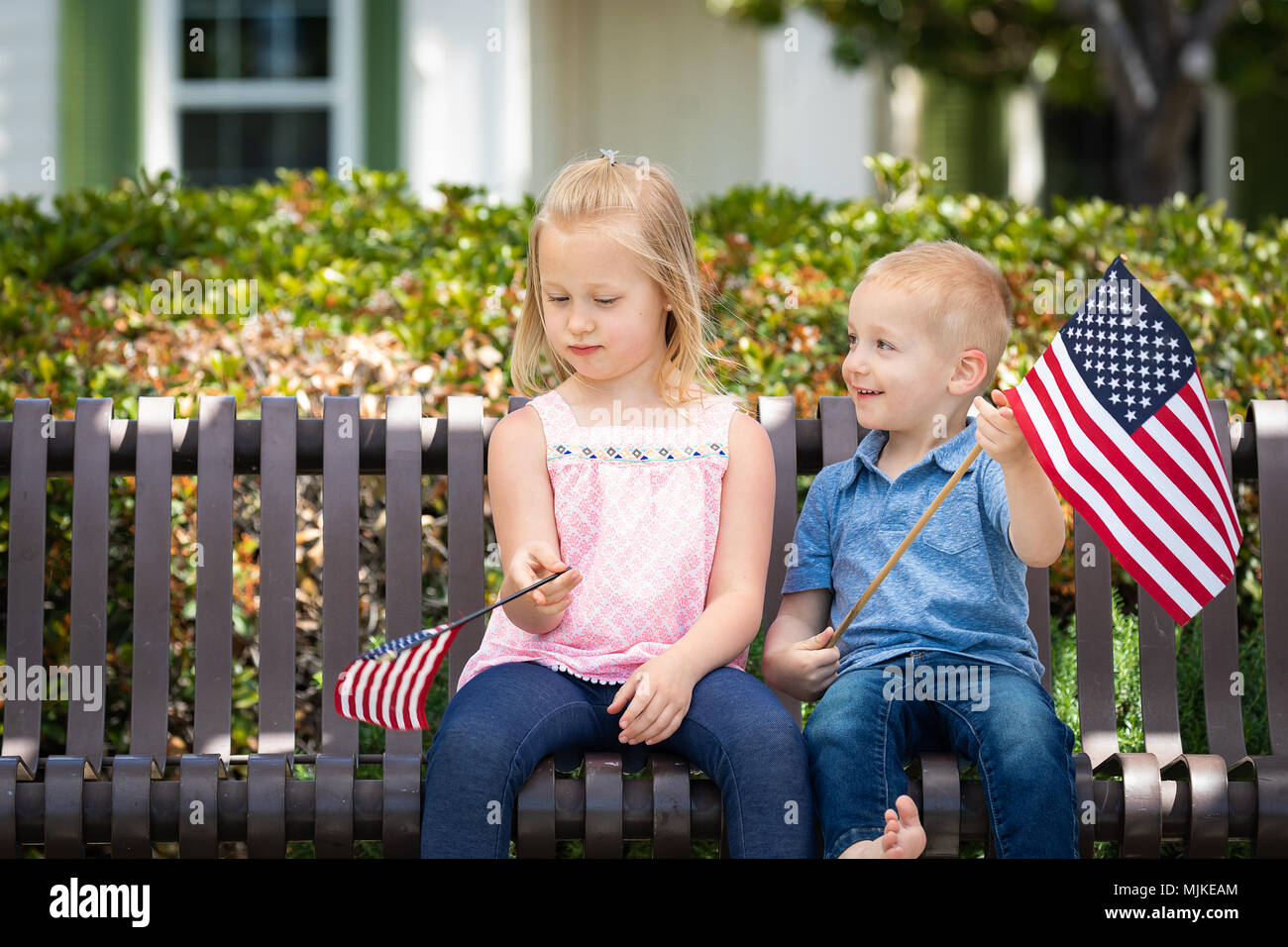 Junge Schwester und Bruder Vergleichen jede andere amerikanische Flagge Größe Auf der Bank im Park. Stockfoto