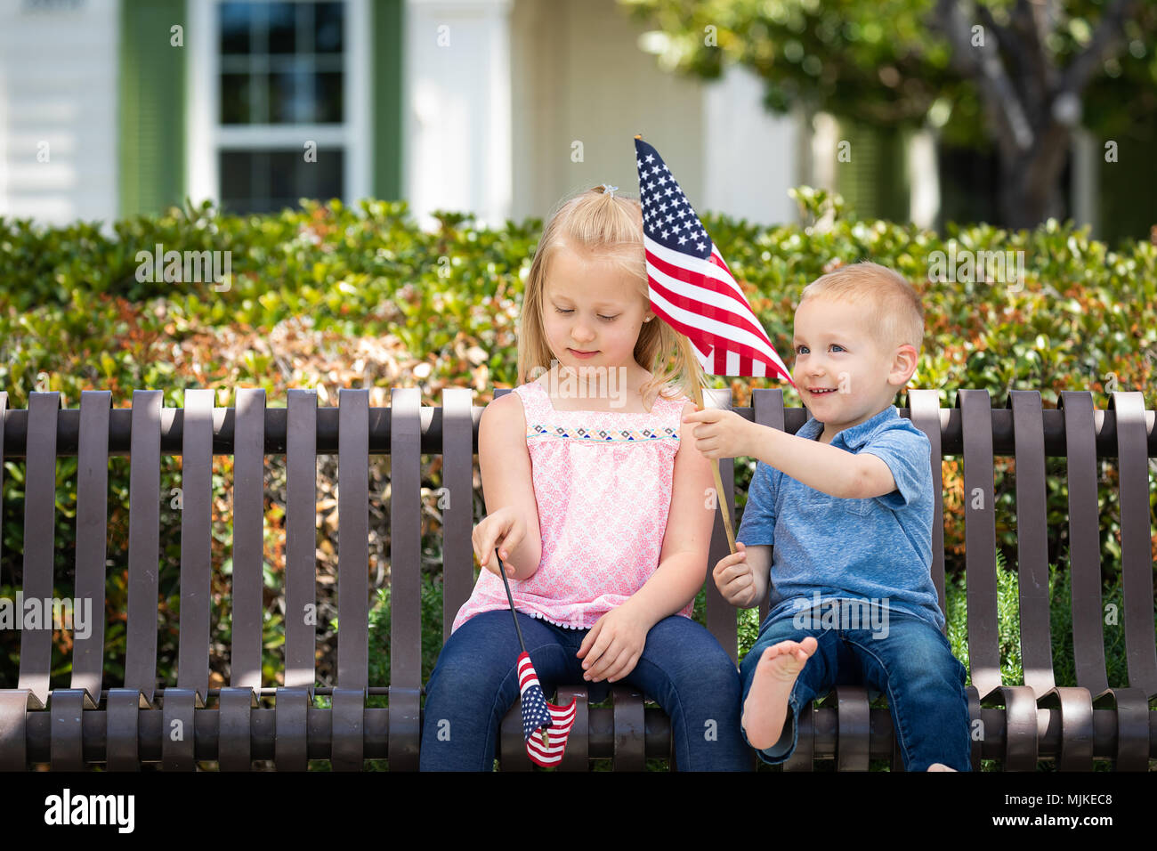 Junge Schwester und Bruder Vergleichen jede andere amerikanische Flagge Größe Auf der Bank im Park. Stockfoto