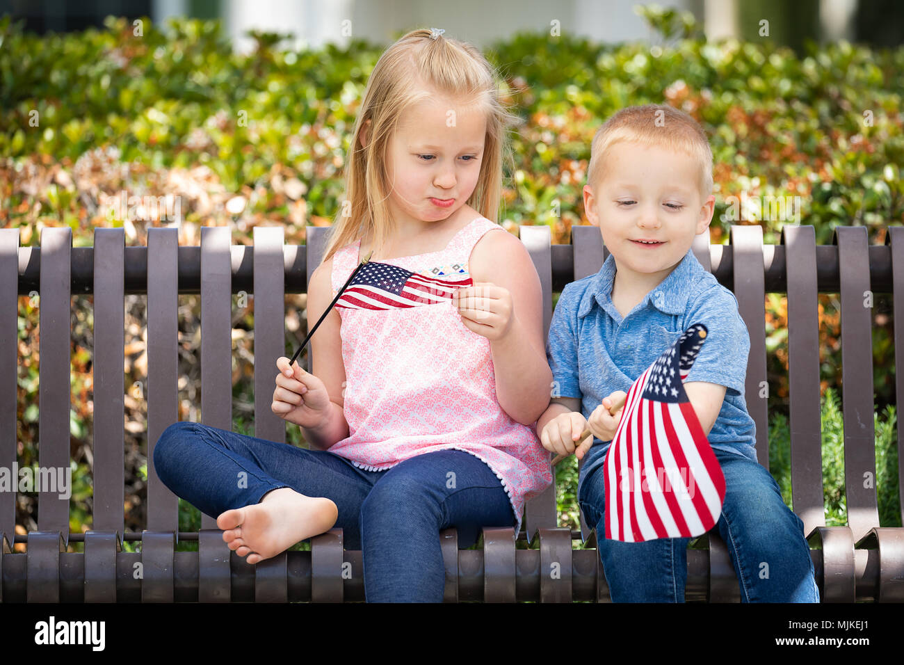 Junge Schwester und Bruder Vergleichen jede andere amerikanische Flagge Größe Auf der Bank im Park. Stockfoto