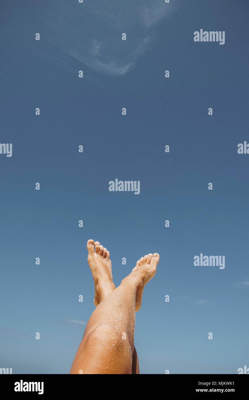 Weibliche Füße im weißen Sand auf blauen Himmel Hintergrund Stockfoto