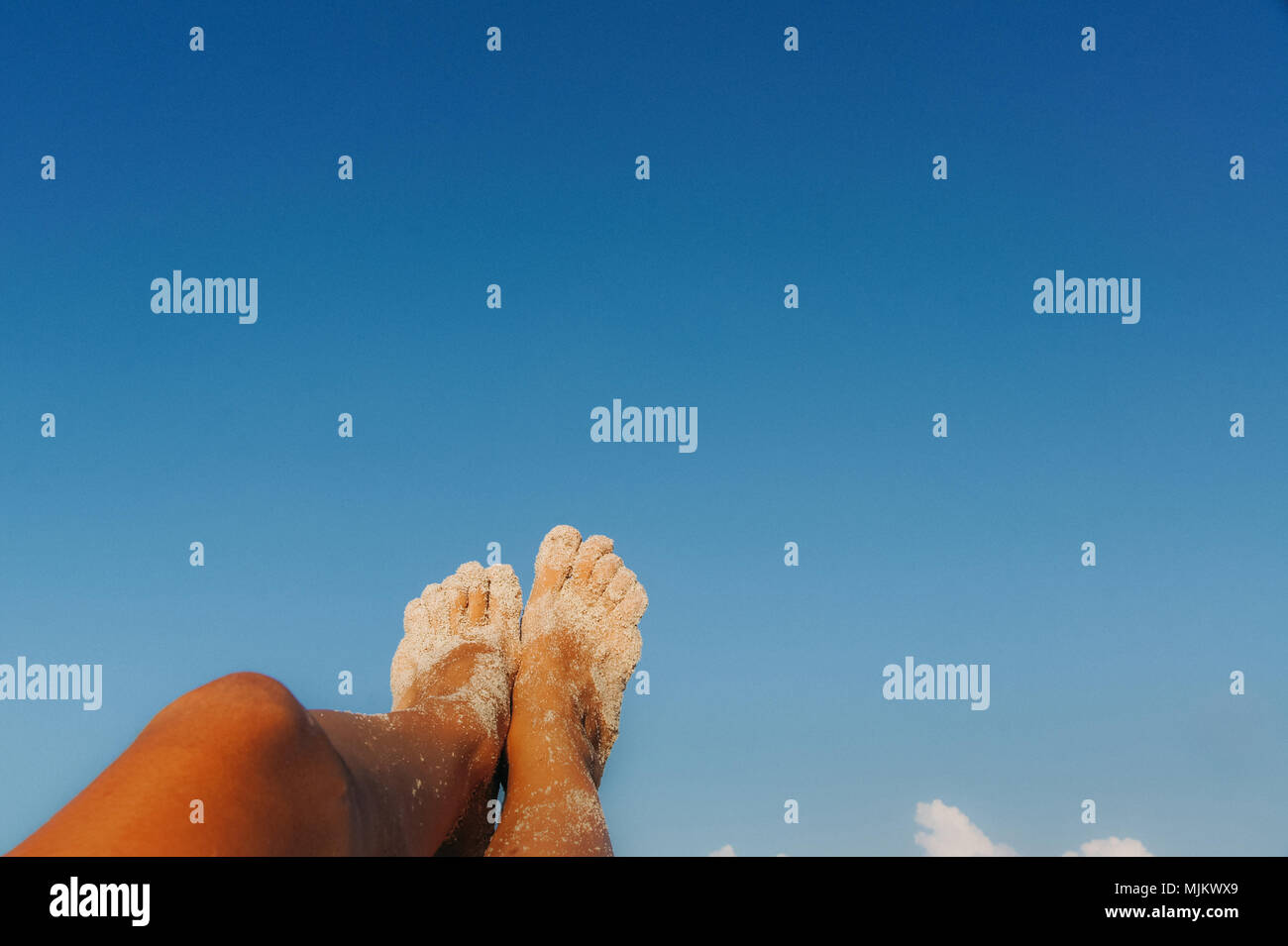 Tan weibliche Füße im weißen Sand auf blauen Himmel Hintergrund Stockfoto