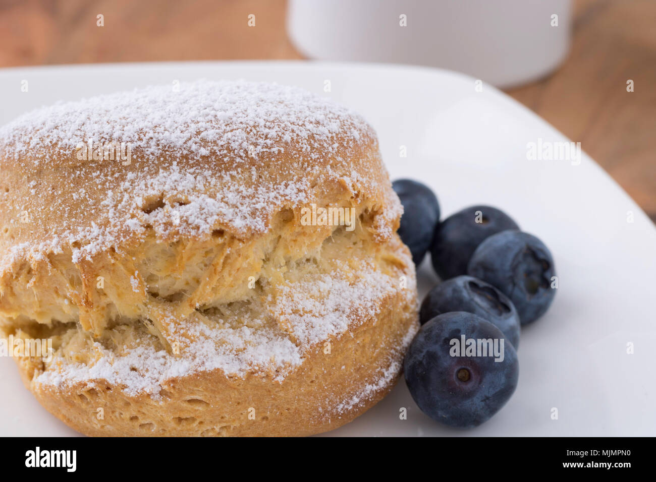 Traditionelle britische Scone auf einem weissen Teller, fünf Blaubeeren auf der rechten Seite, British Tea Time Stockfoto