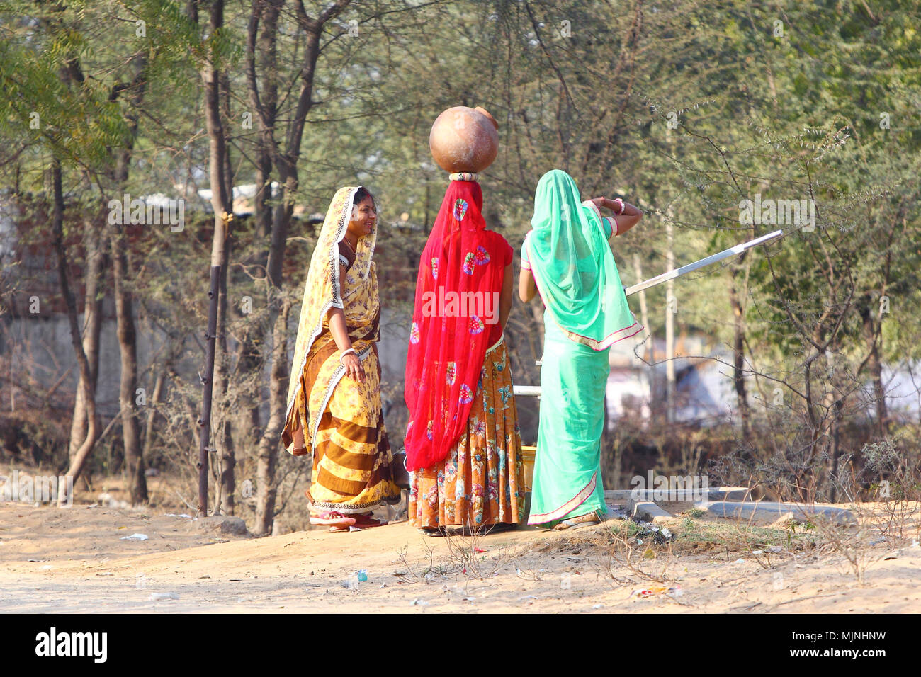 DAHMI KALAN - Indien, Januar 13, 2018: Drei junge Rajasthani Frauen in bunten Saris diskutieren in der Nähe von einem Brunnen beim Füllen der Krüge mit Wasser Stockfoto