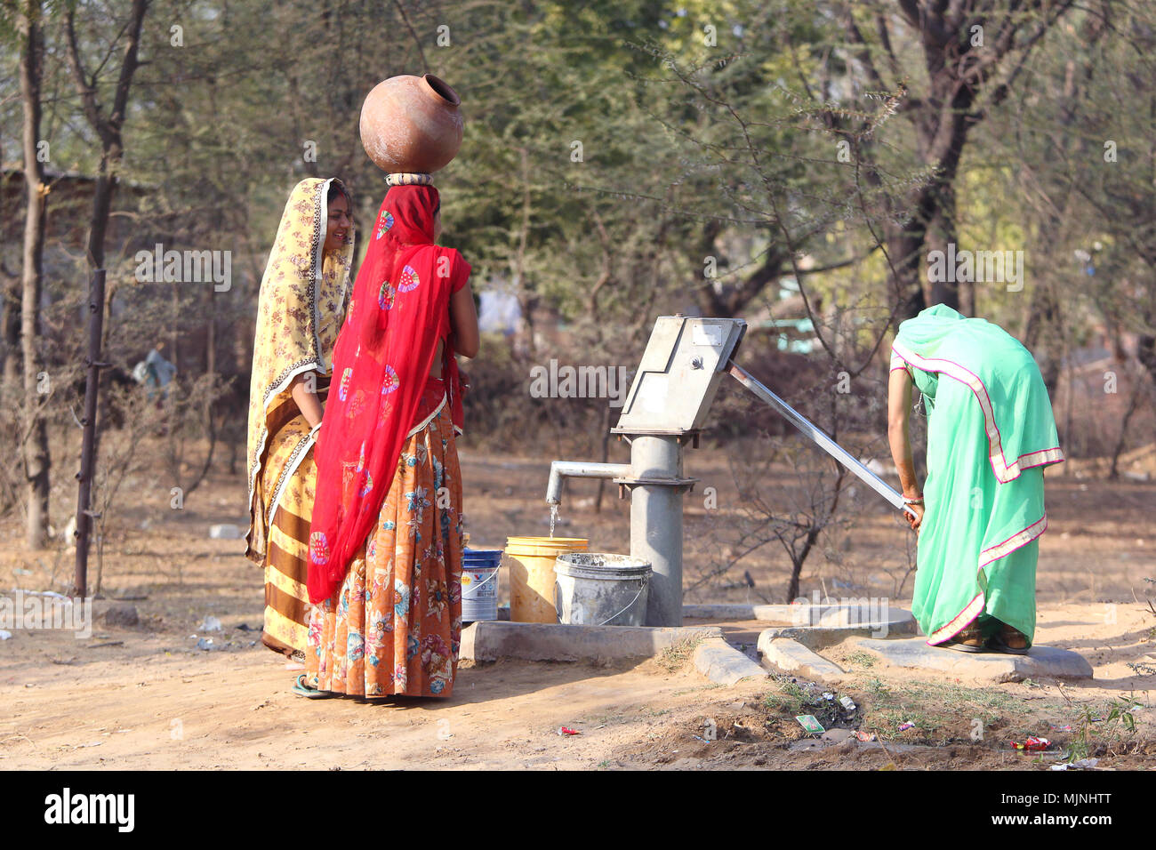 DAHMI KALAN - Indien, Januar 13, 2018: Drei junge Rajasthani Frauen in bunten Saris diskutieren in der Nähe von einem Brunnen beim Füllen der Krüge mit Wasser Stockfoto