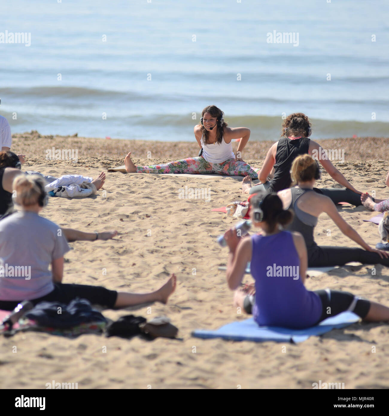Morgen Sonnenschein an der Südküste auf die heißesten Mayday Bank Holiday Wochenende auf Aufzeichnung in Boscombe, Bournemouth, Dorset, UK, Mai 2018. Eine Gruppe von Frauen an einem Yoga Training und Stretching Klasse am Strand. Stockfoto