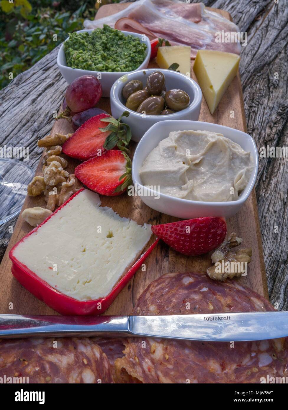 Verkostung Teller mit Käse, Salami, Erdbeeren, Oliven, Nüsse, Humus und Prosciutto auf Holzbrett sitzen auf verwitterte Zaun Geländer. Stockfoto