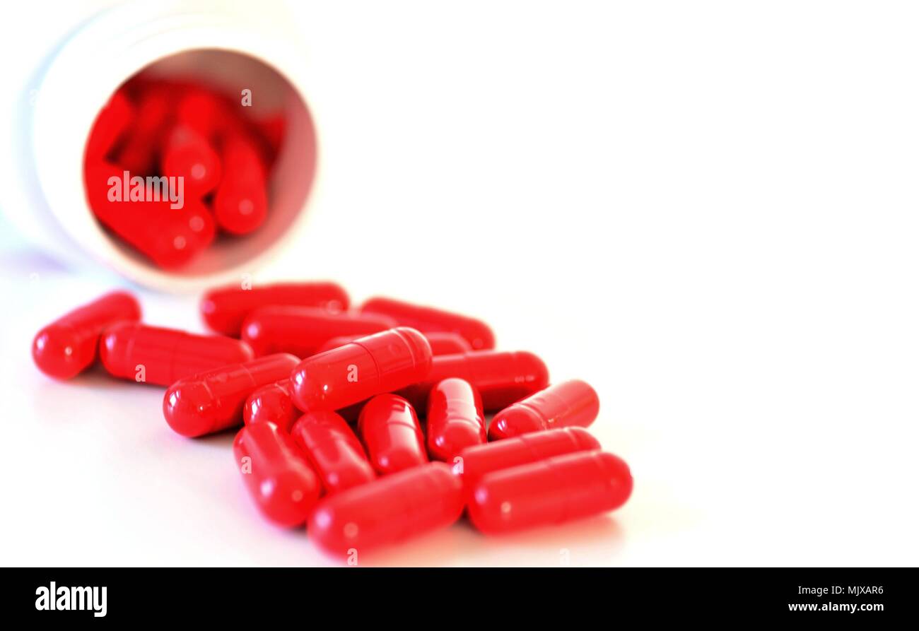 Rote Kapseln Flüssigkeit aus einem Behälter auf weißem Hintergrund. Stockfoto