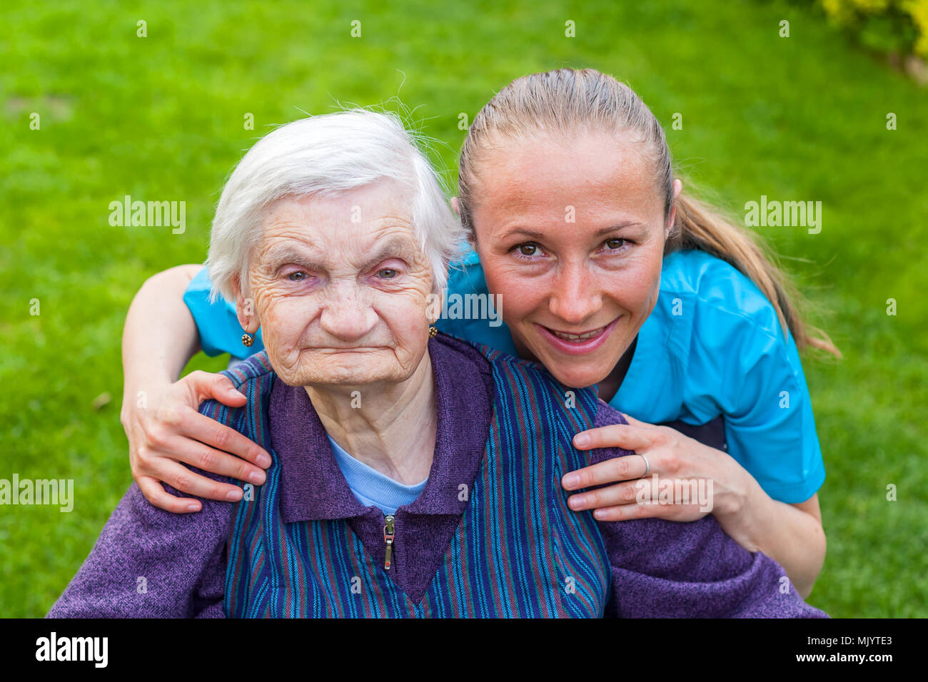 Portrait von ältere behinderte Frau in einem Rollstuhl verbringen Zeit im Freien mit fröhlichen jungen Betreuer Sitzung Stockfoto