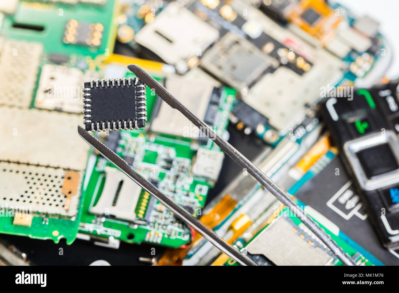 Elektronische chip in Pinzette auf dem Hintergrund der demontierten Mobiltelefon Stockfoto