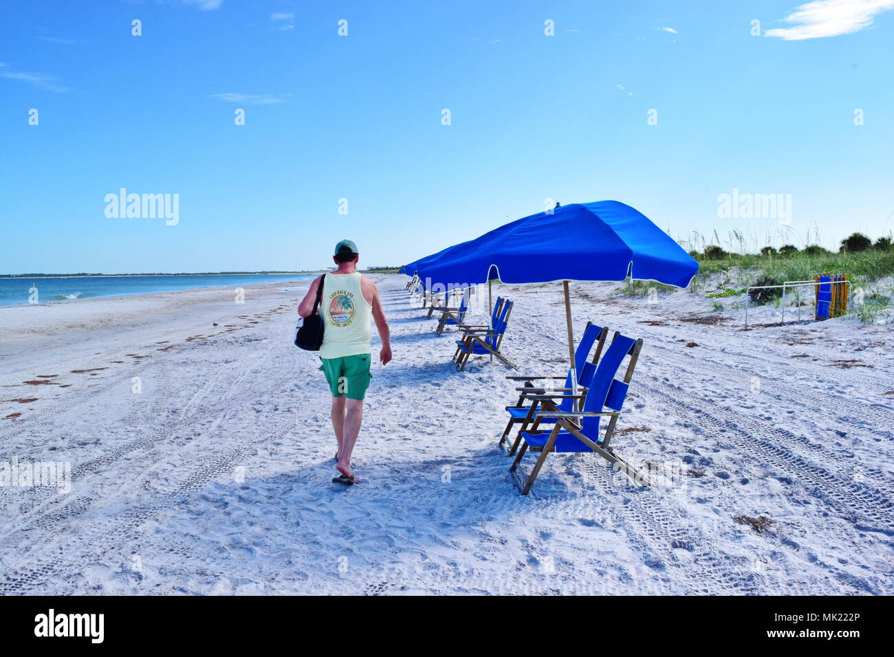 Zurück von Mensch zu Fuß die weißen Sandstrand auf der Caladesi Island State Park in Florida auf hellen, sonnigen Tag mit Sonnenschirme und Stühle für Touristen. Stockfoto