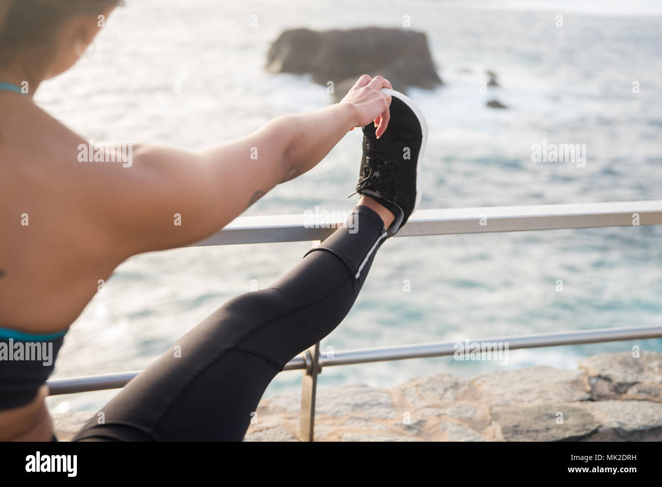 Die Frau, die durch das Meer mit Bein auf dem Geländer und Hände berühren Zehen trägt schwarze Strumpfhosen und Sneakers Stockfoto