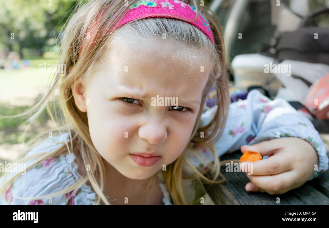 Böse Mädchen Holding Karotte am Picknicktisch - weigert zu essen 5-a-day oder Healthy-Eating Stockfoto
