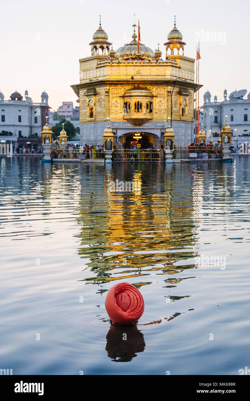 Amritsar, Punjab, Indien: ein Sikh Mann nimmt ein heiliges Bad an der Amrit Sarovar (Pool von Nektar) der Goldene Tempel beleuchtet in der Abenddämmerung. Stockfoto