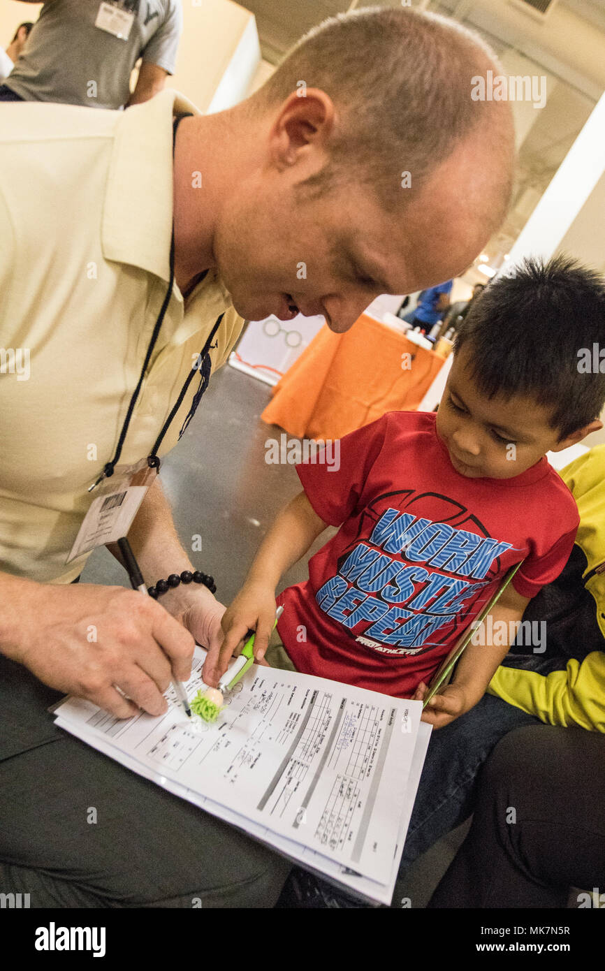 Us-Armee finden Sgt. Brendan Irland, ein optometrie Techniker, geht über einen Vision-fitness test mit Justin Vasquez, 3, in der Betreuung Hafen in Los Angeles, Calif., Nov. 18, 2017. Irland, ist eines von Dutzenden von Armee-reserve Soldaten aus der 7214Th medizinische Unterstützung in Los Alamitos, Calif., stationiert, die ihre Zeit und ihren medizinischen Know-how freiwillig helfen Kostenlose Versorgung für die Bürger von Los Angeles bieten; viele von ihnen haben keinen Zugang zu medizinischer Versorgung. (U.S. Armee Foto: Staff Sgt. Felix R. Fimbres) Stockfoto