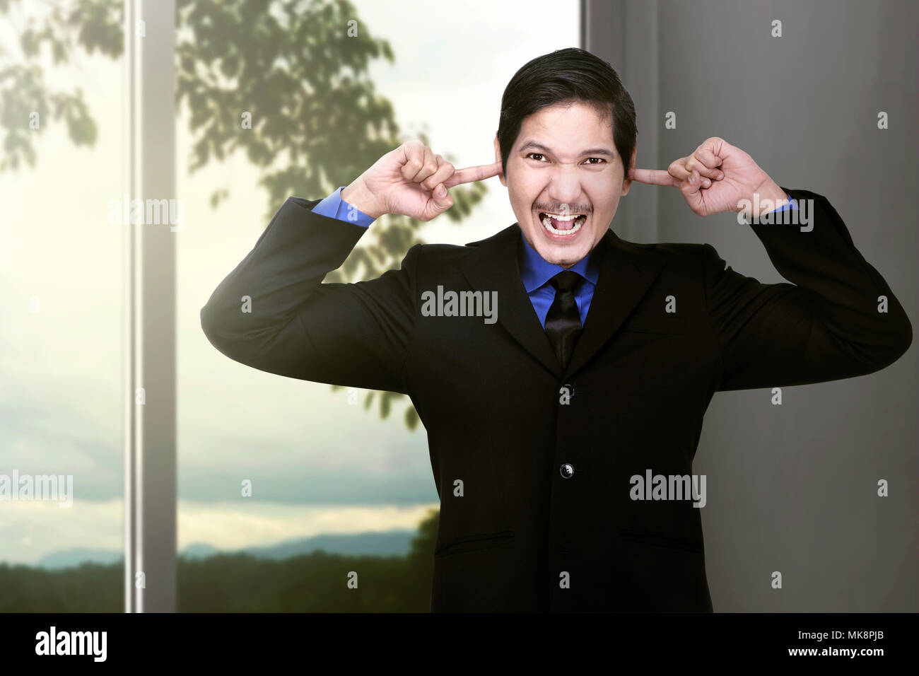 Unglücklich asiatische Geschäftsmann für seine Ohren nicht großartig Lärm zu Hause hören Stockfoto