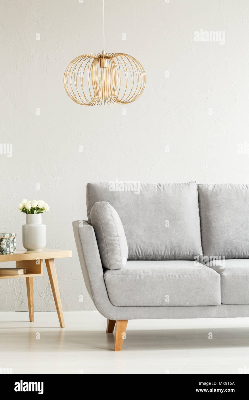 Gold Lampe über grau Couch neben einem Holztisch mit weißen Blüten im Wohnzimmer Innenraum Stockfoto