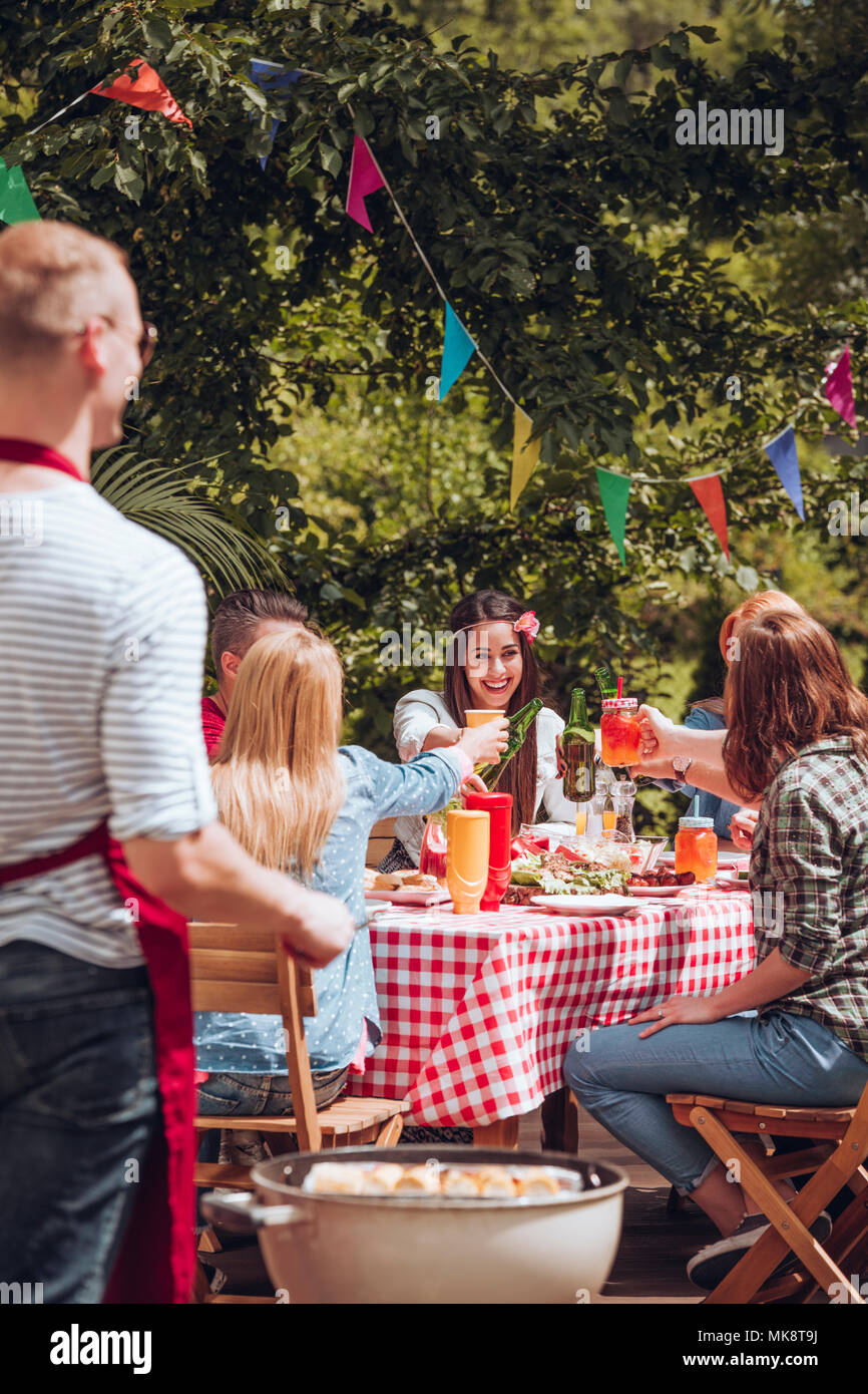 Lächelnde Frau Toasten mit Freunden an einem Tisch mit gegrillten Speisen während der Geburtstagsfeier Stockfoto