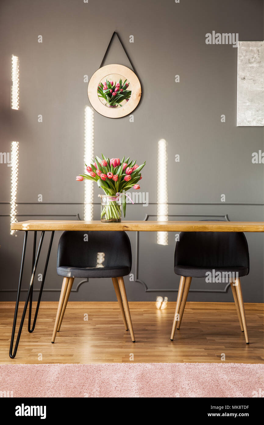 Stühle an den hölzernen Tisch mit Blumen gegen graue Wand mit Dekor in femininen Esszimmer Innenraum Stockfoto