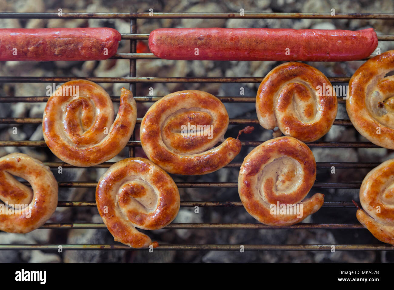 Gegrillte Würstchen auf den brennenden Grill. Cumberland Wurst, Spirale Wurst aus Schweinefleisch auf BBQ Grill, hausgemachte. Grill Würstchen auf dem Grill. Verschiedene Sorten von Sa Stockfoto