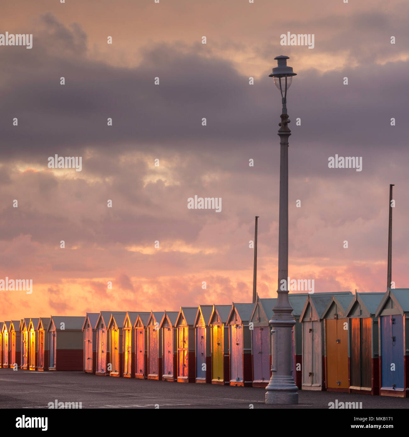 Farbenfrohe Strandhütten an der Küste von Hove, East Sussex, die im goldenen Licht des Sonnenuntergangs unter einem dramatischen Himmel leuchten. Stockfoto