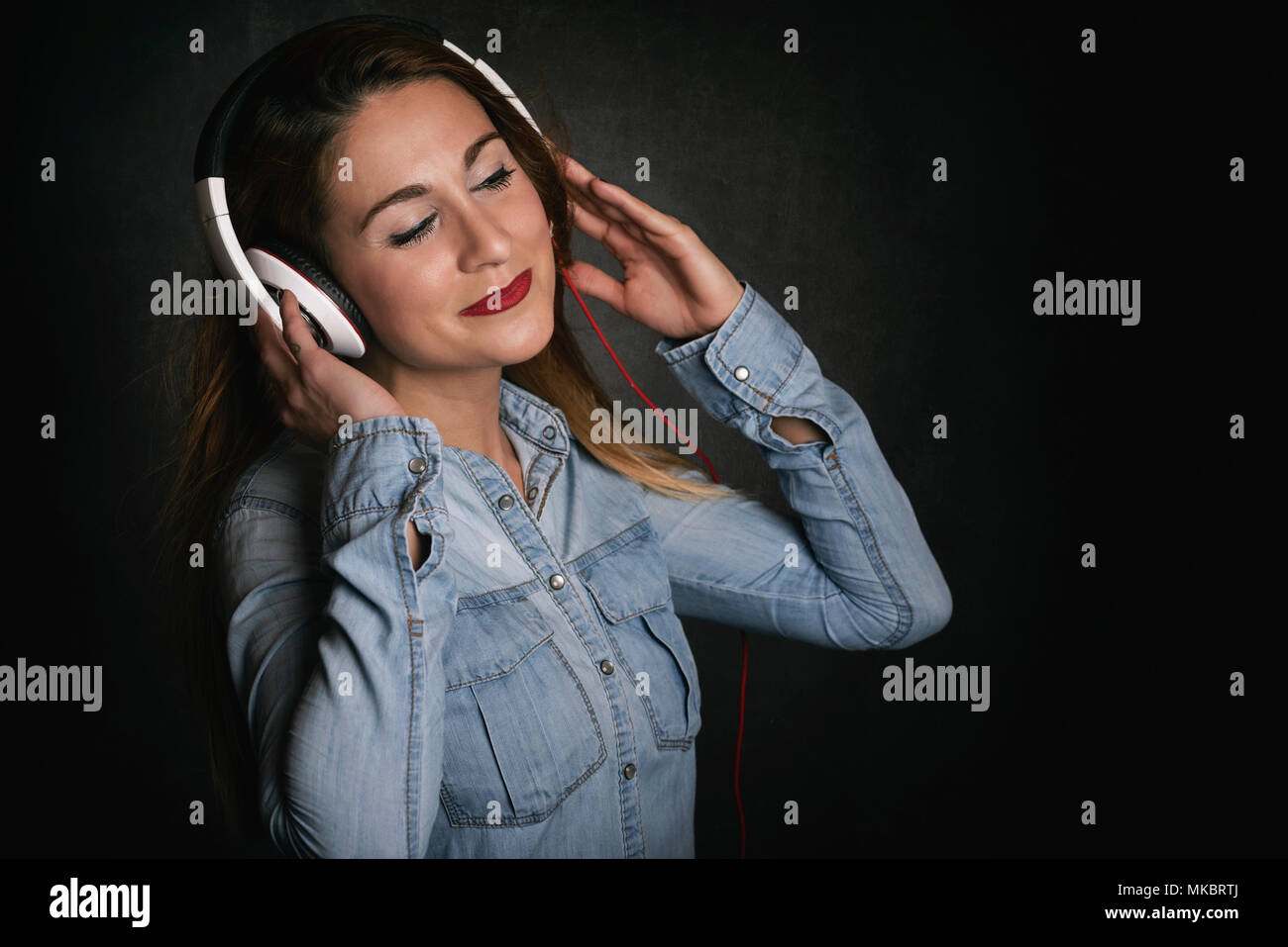 Glückliche junge Frau mit Kopfhörer auf schwarzem Hintergrund Stockfoto