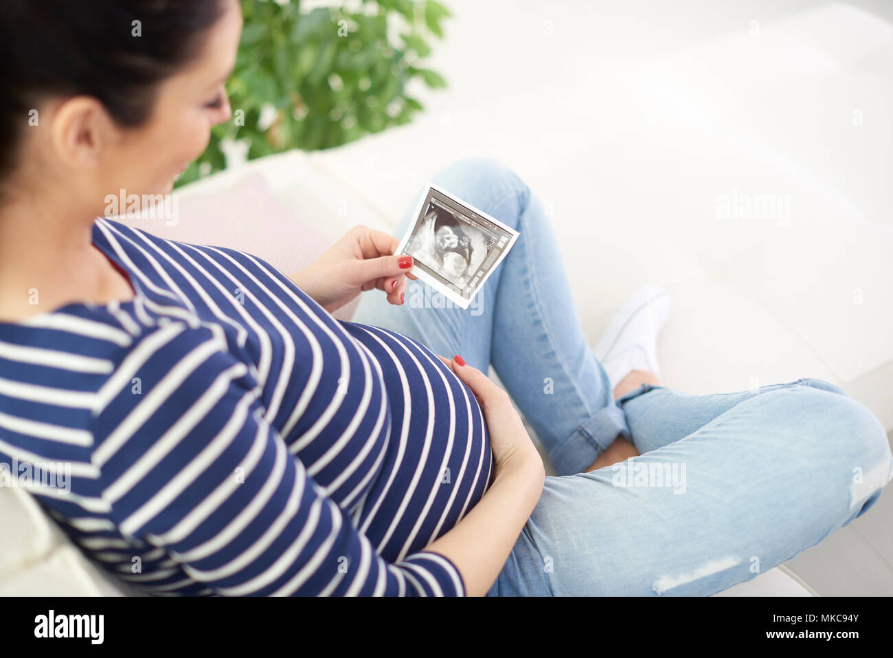 Hohe Aufnahme von glücklichen schwangeren Frau die Hand 3D-Ultraschallbild Ihres Babys beim Entspannen auf dem Sofa. Stockfoto