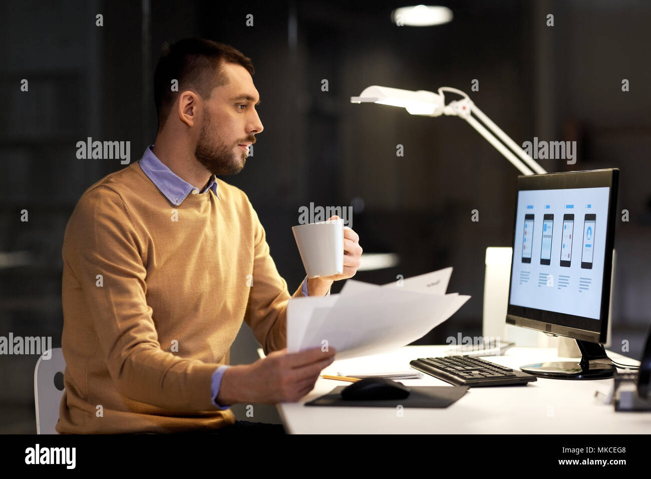 Mann mit Papieren und Computer funktioniert bei Nacht Büro Stockfoto