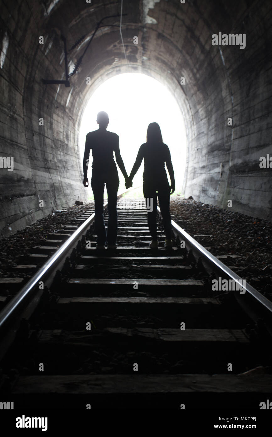 Paar Hand in Hand entlang der Strecke durch eine Eisenbahn Tunnel Richtung helles Licht am anderen Ende, erscheinen sie als Silhouetten gegen die Stockfoto
