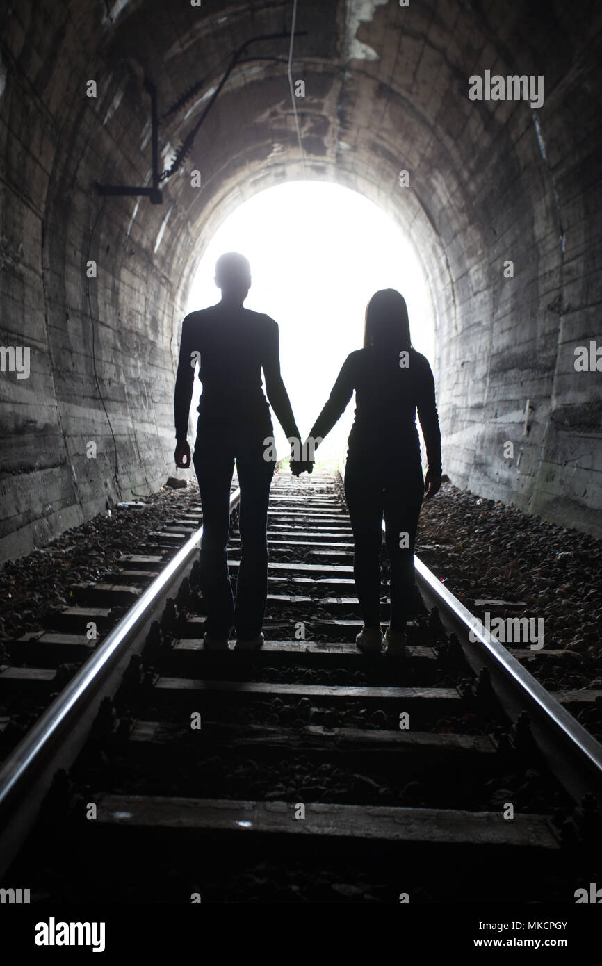 Paar Hand in Hand entlang der Strecke durch eine Eisenbahn Tunnel Richtung helles Licht am anderen Ende, erscheinen sie als Silhouetten gegen die Stockfoto