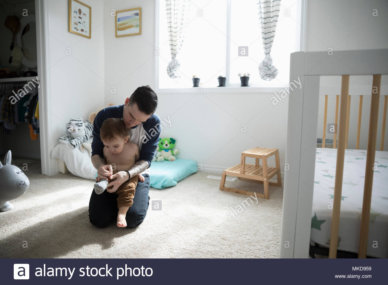 Vater Dressing, Putting Socken auf Baby Sohn im Kindergarten Stockfoto