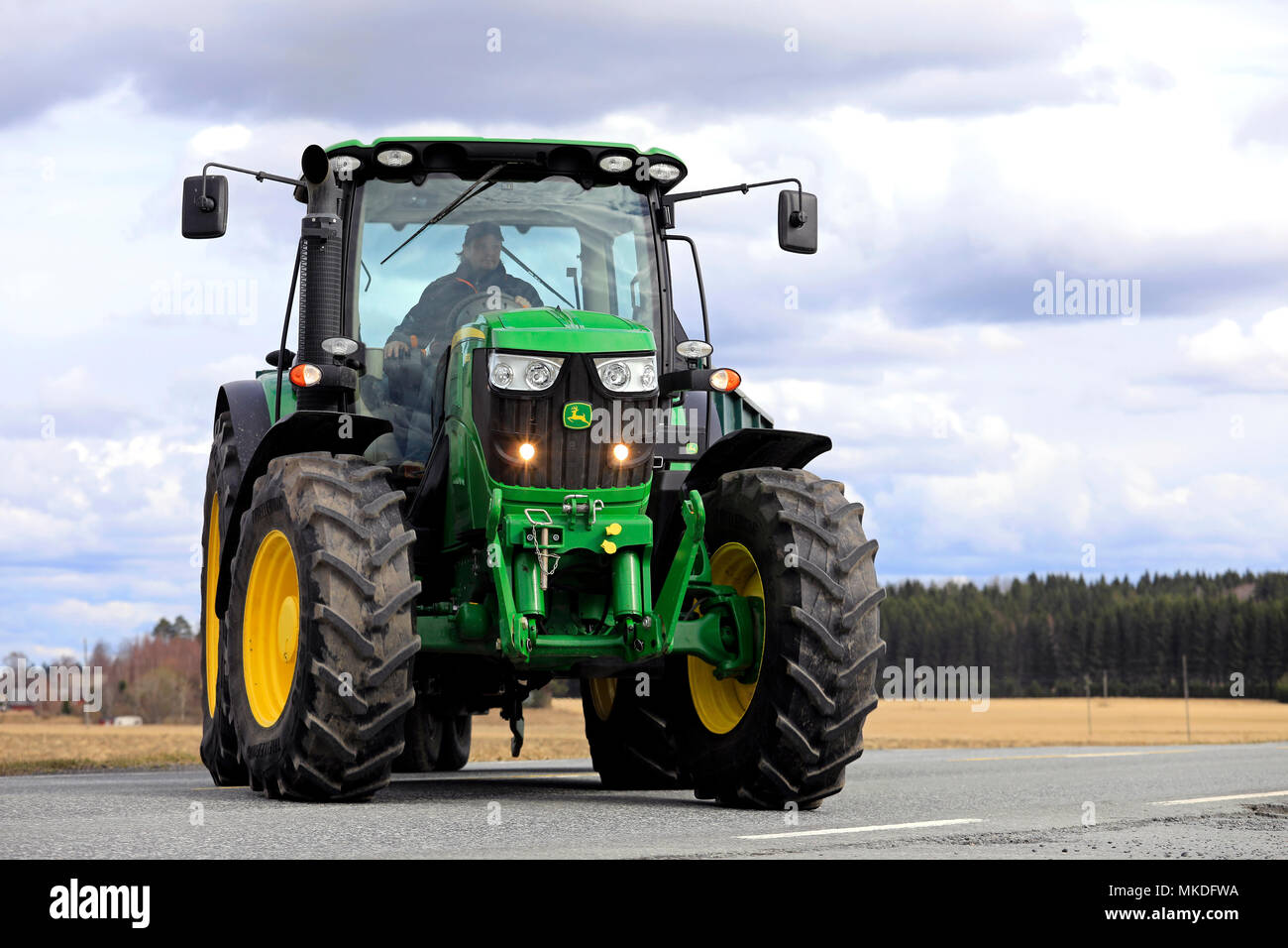 Bauer macht eine Rechtskurve mit John Deere 6150R Traktoren und landwirtschaftliche Anhänger an der Hauptstraße. Jokioinen, Finnland - 30. April 2018. Stockfoto