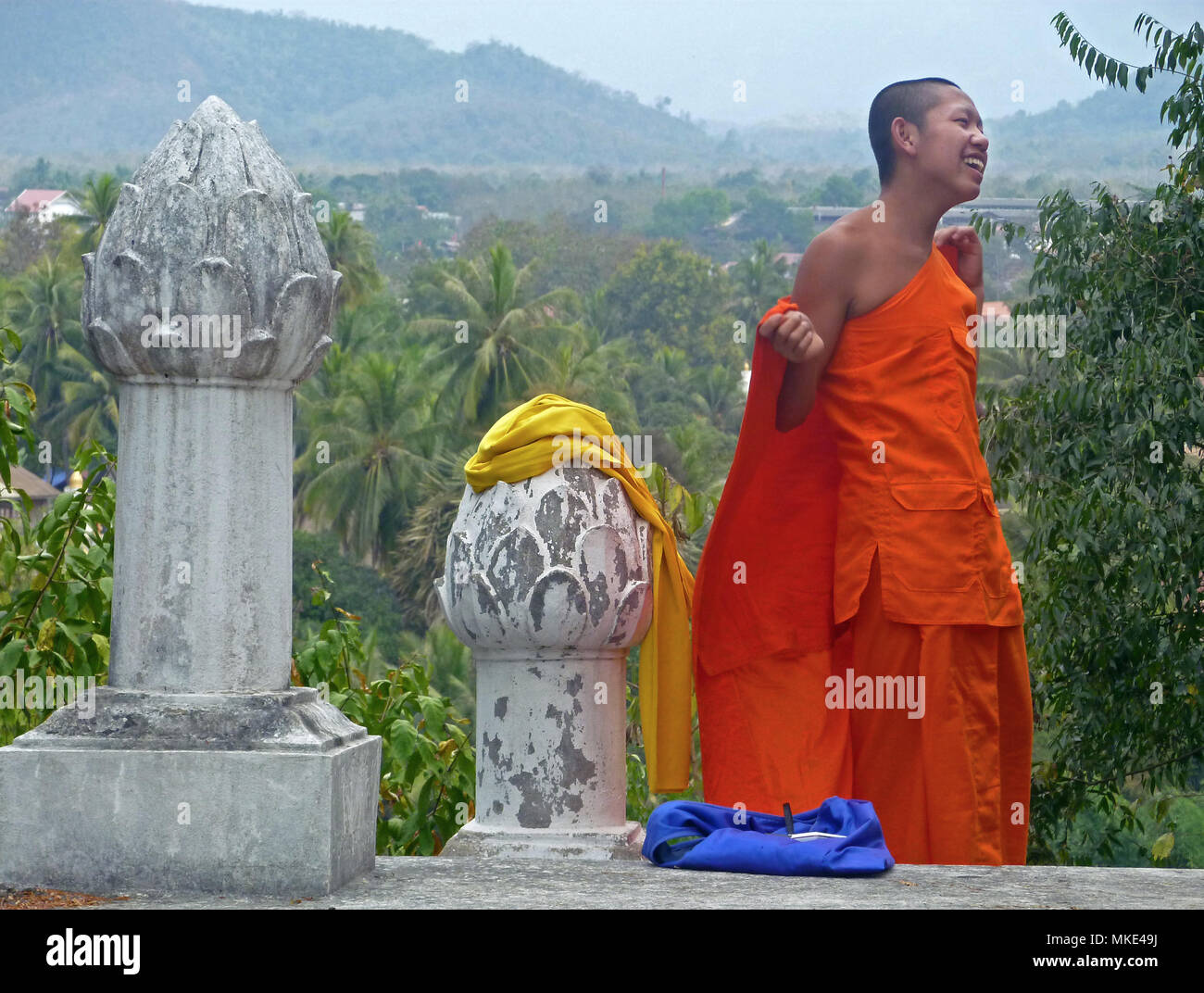 Ein buddhistischer Mönch mit orangefarbenen Robe steht auf einem Hügel mit Lotus Stammzellen Schnitzereien. Stockfoto