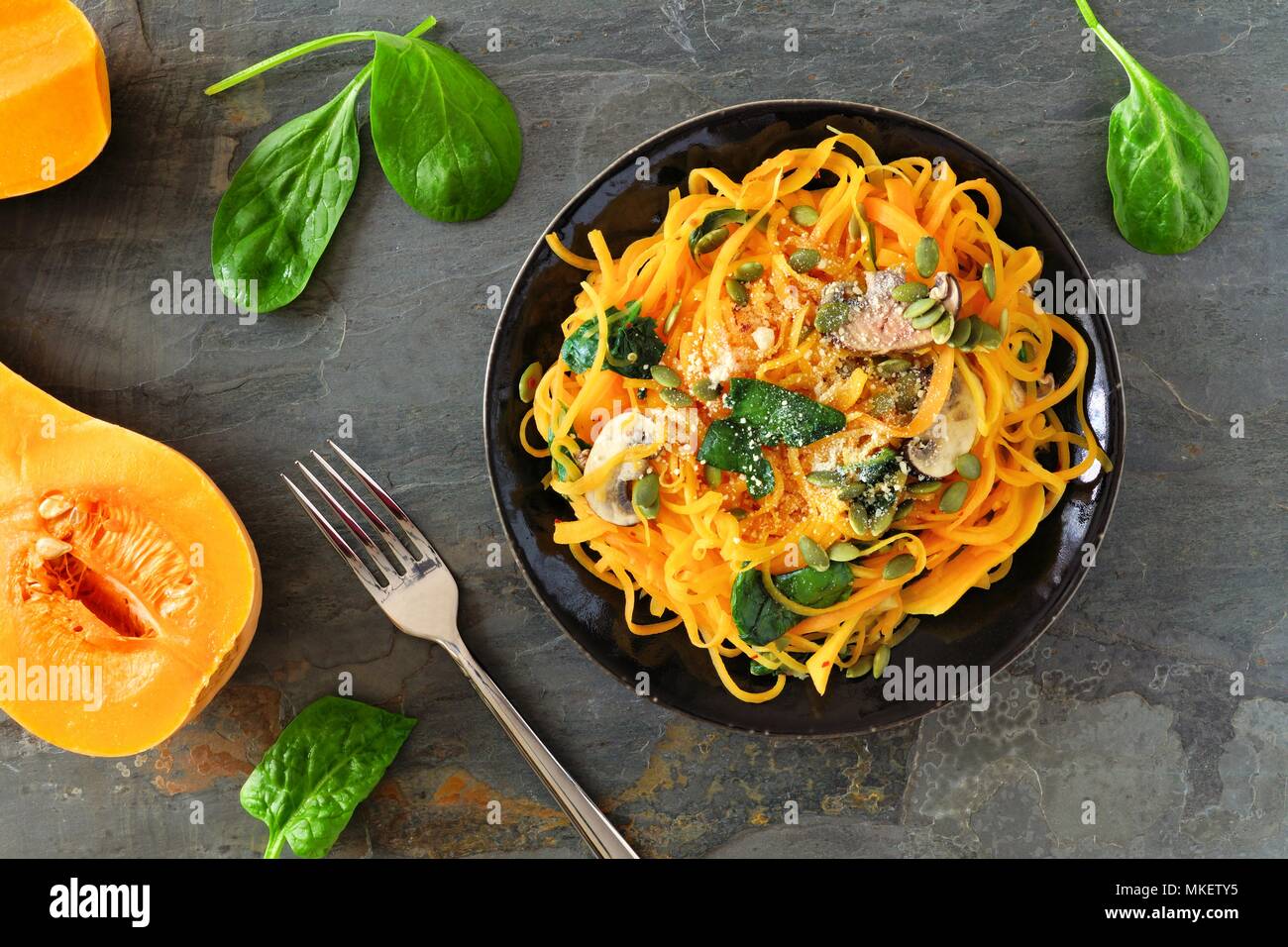 Butternut-kürbis spirilized Nudeln mit Spinat und Kürbiskerne auf dunklem Schiefer Hintergrund, gesunde Ernährung Konzept. Ansicht von oben, Tabelle Szene. Stockfoto