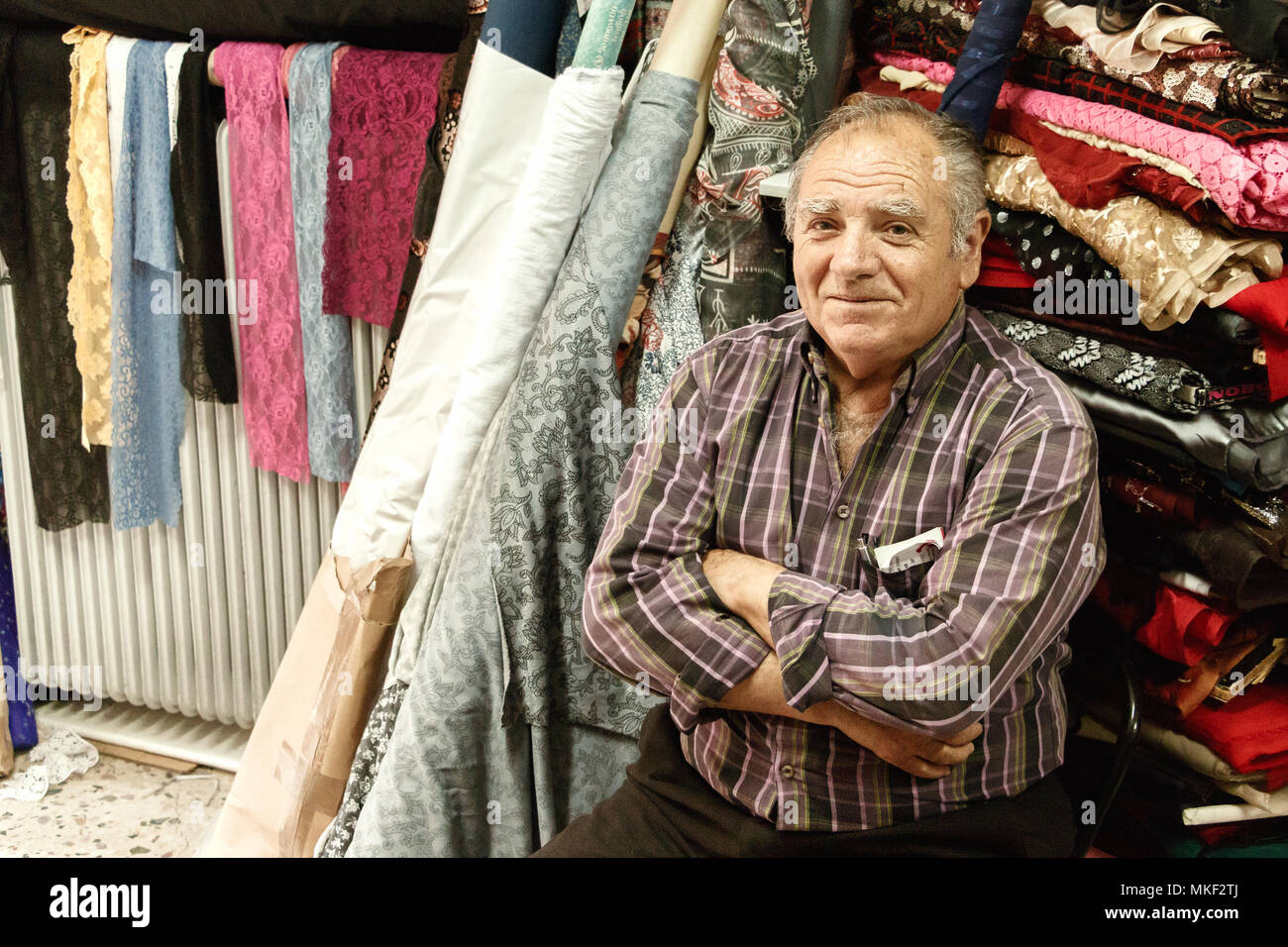 Larissa, Thessalien, Griechenland - Mai 4., 2018: Portrait eines älteren Mannes in seinem Stoff store in Skiathos Stadt, Griechenland entfernt sitzen. Stockfoto Larissa, Thessalien, Griechenland - Mai 4., 2018: Portrait eines älteren Mannes in seinem Stoff store in Skiathos Stadt, Griechenland entfernt sitzen. Stockfoto