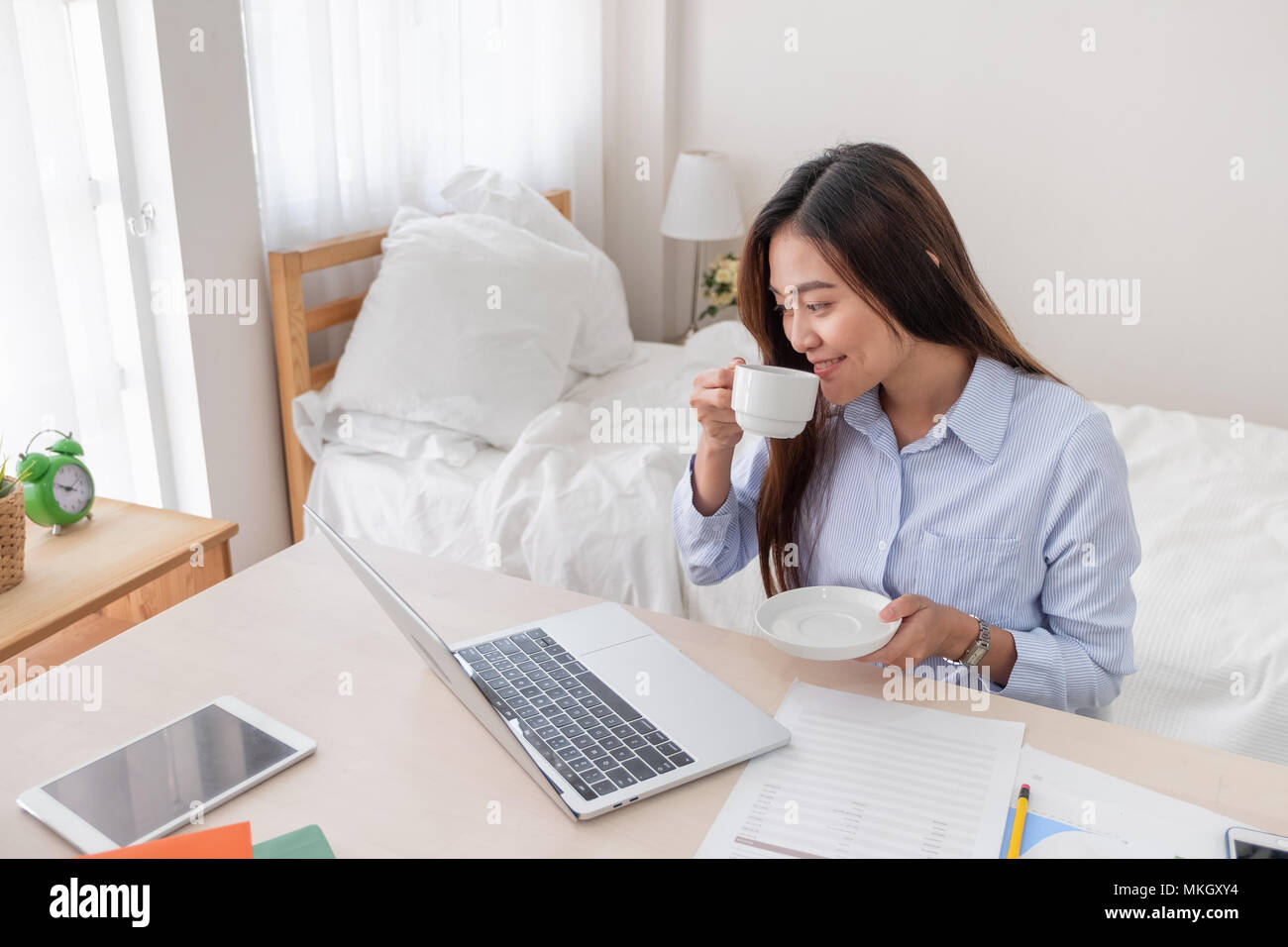 Asiatische Geschäftsfrau Kaffee trinken und während der Arbeit mit dem Laptop auf dem Tisch im Schlafzimmer zu Hause. Arbeit zu Hause Konzept. Arbeiten von zu Hause Konzept Stockfoto