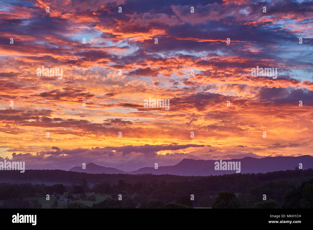 Ein dramatischer Sonnenuntergang wie die Sonnen Lichts auf Wolken kurz nach Sonnenuntergang mit dem Great Dividing Range im Hintergrund von Repton, Australien Stockfoto