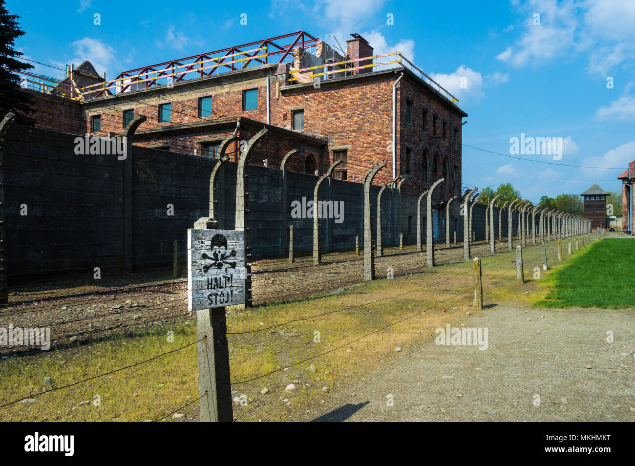 Stoj!' 'Halt, STOP-Schild mit Totenkopf in Auschwitz, die NS-Konzentrationslager in Polen. Landschaft an einem sonnigen Tag mit Gebäuden im Hintergrund. Stockfoto