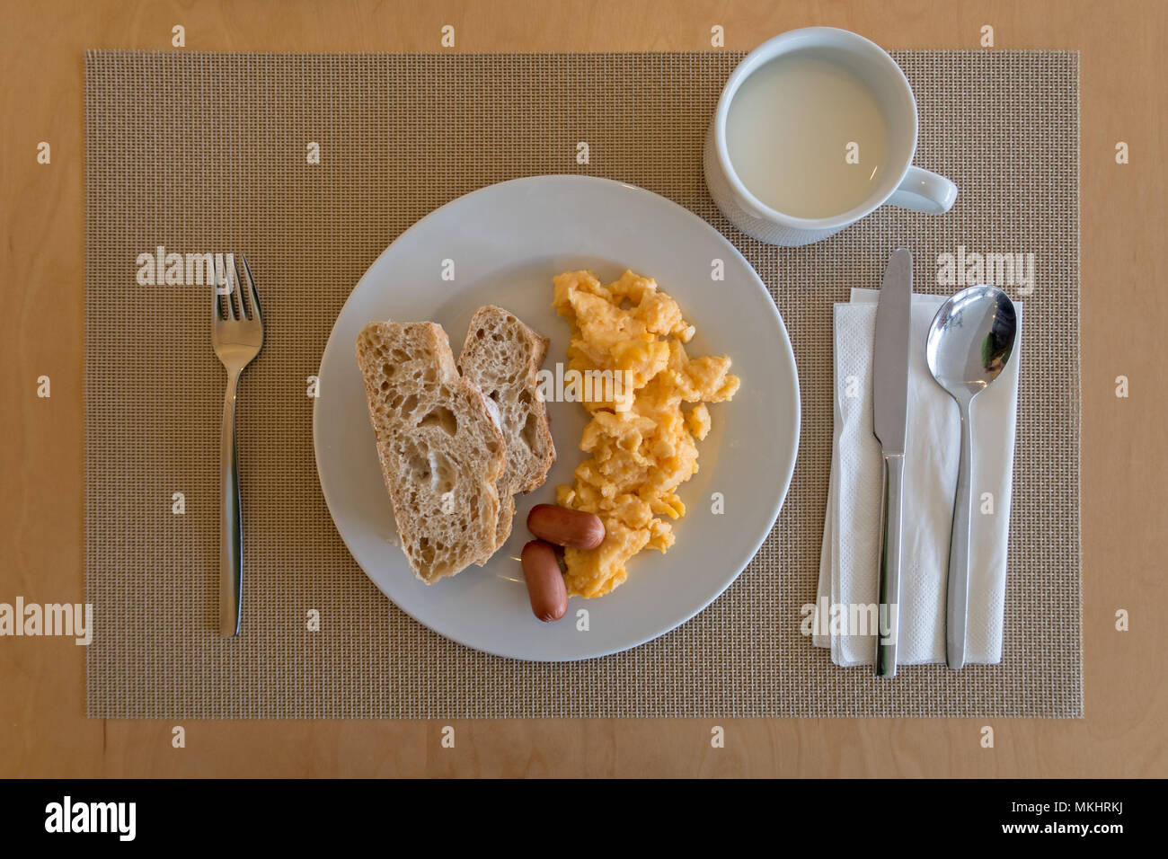 Ansicht von oben ein Frühstück mit Rührei, kleine Würstchen, weißes Brot und eine Tasse Milch Stockfoto