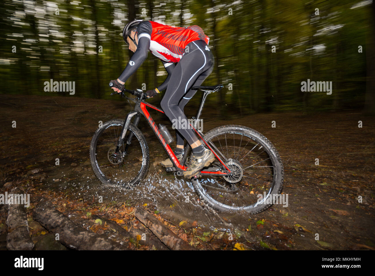 Mountainbiker in dunklen Wiener Wald reitet schnell Offroad auf Carbon hardtail entlang Trail durch den Wald Stream mit Wasser spritzt. Stockfoto