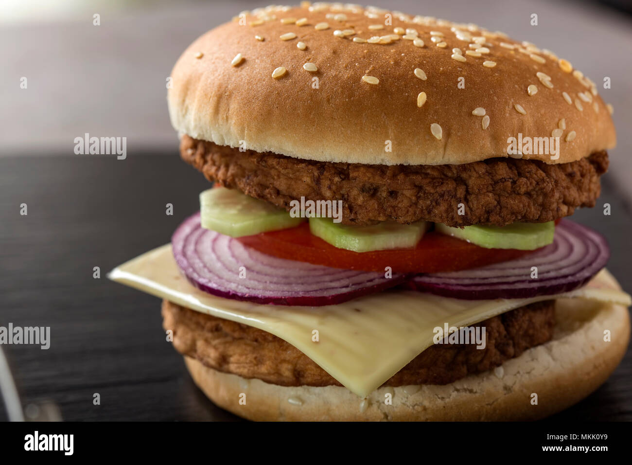 Nahaufnahme eines Cheeseburger mit Tomaten, Zwiebeln und Gurke auf Schiefer Stockfoto