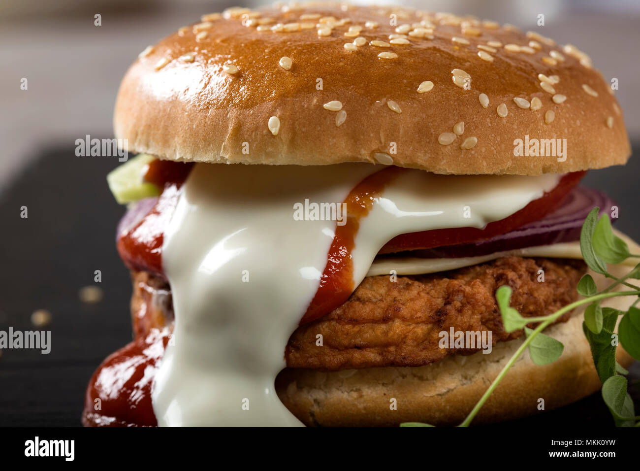 Nahaufnahme von einem Cheeseburger mit Tomaten und Mayonnaise Soße auf Schiefer Stockfoto