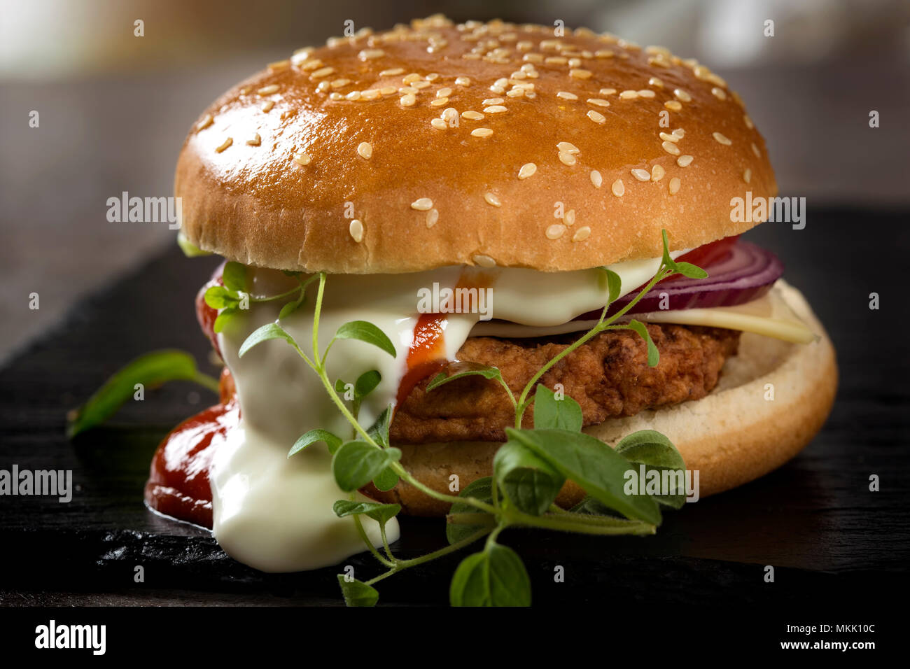 Nahaufnahme von einem Cheeseburger mit Tomaten und Mayonnaise Soße auf Schiefer mit grün Oregano Stockfoto