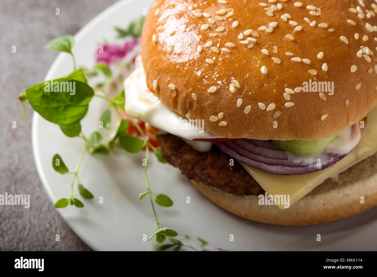 Blick von oben auf einen Cheeseburger mit Tomaten und Mayonnaise Sauce auf dem Teller mit grünen Oregano Blätter Stockfoto