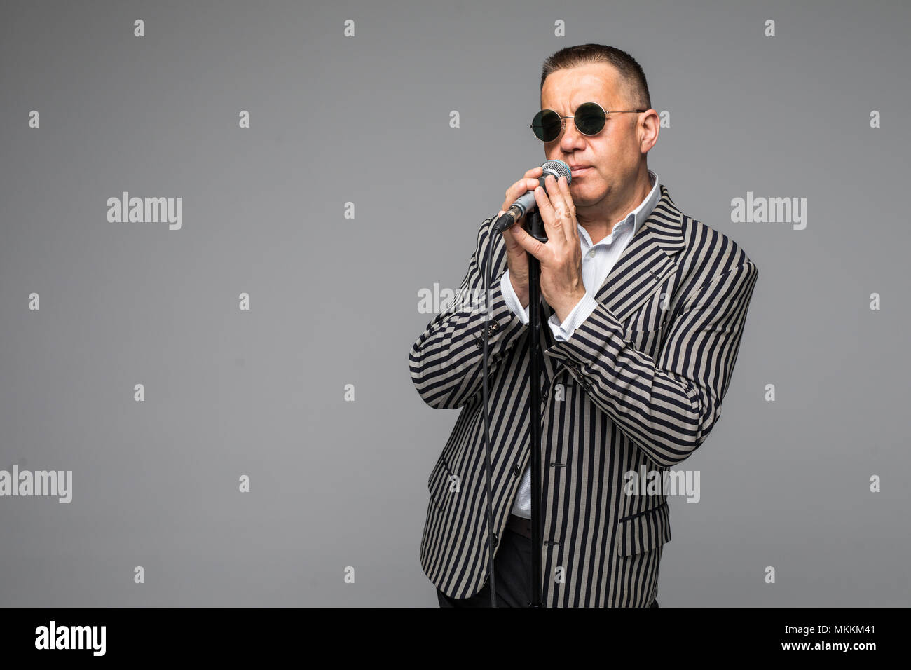 Das mittlere Alter Showman Interviewer mit Emotionen. Junge elegante reifer Mann mit Mikrofon gegen den weißen Hintergrund. Stockfoto