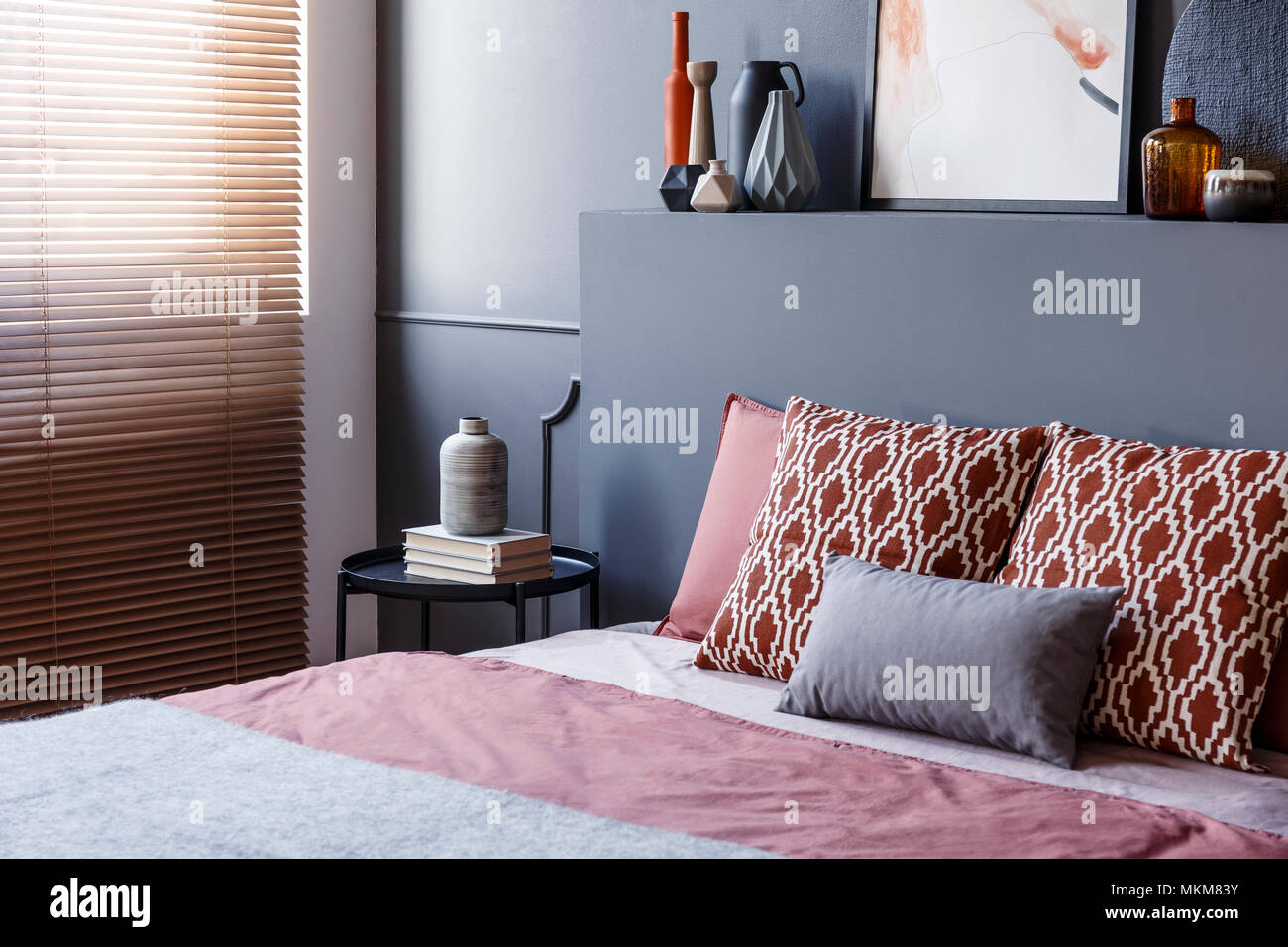 Nahaufnahme der gemusterten Kissen liegend auf einem weichen Bett im Schlafzimmer Innenraum mit schwarzen Wänden, dekorative Vasen und braunen Jalousien. Real Photo Stockfoto
