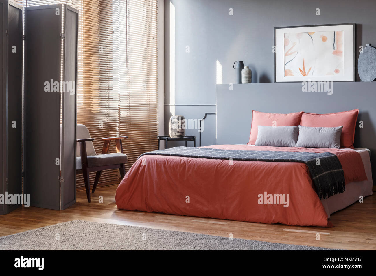 Echten Foto von eleganten Schlafzimmer Innenraum mit schwarzen Wänden, braunen Jalousien und orange Blätter auf grau Bed Stockfoto