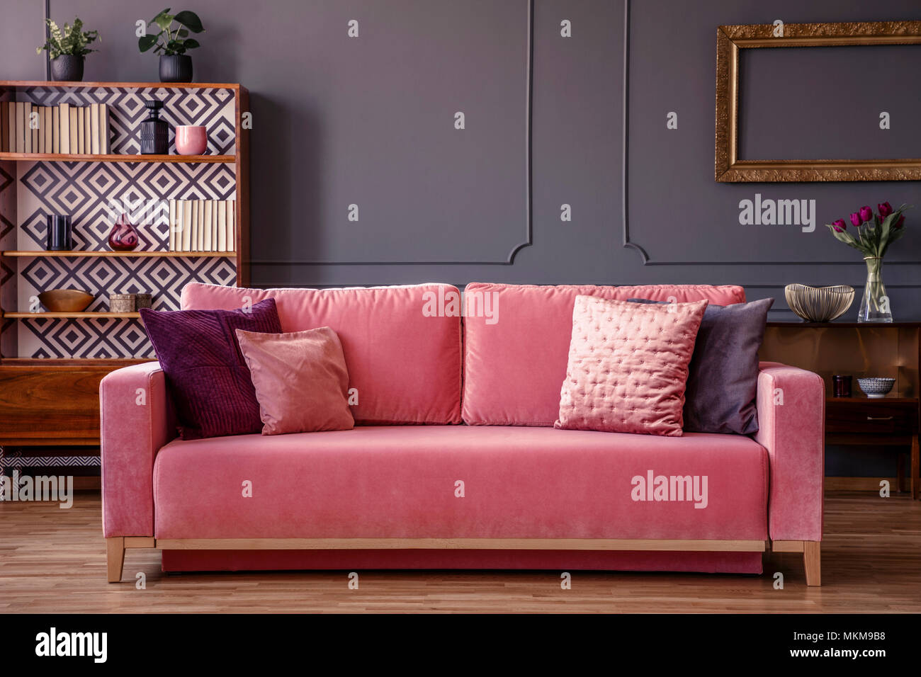 Rosa Samt Couch mit dekorativen Kissen in grau Wohnzimmer Interieur mit Vintage wandschrank, frische Pflanzen und Gießen an der Wand Stockfoto