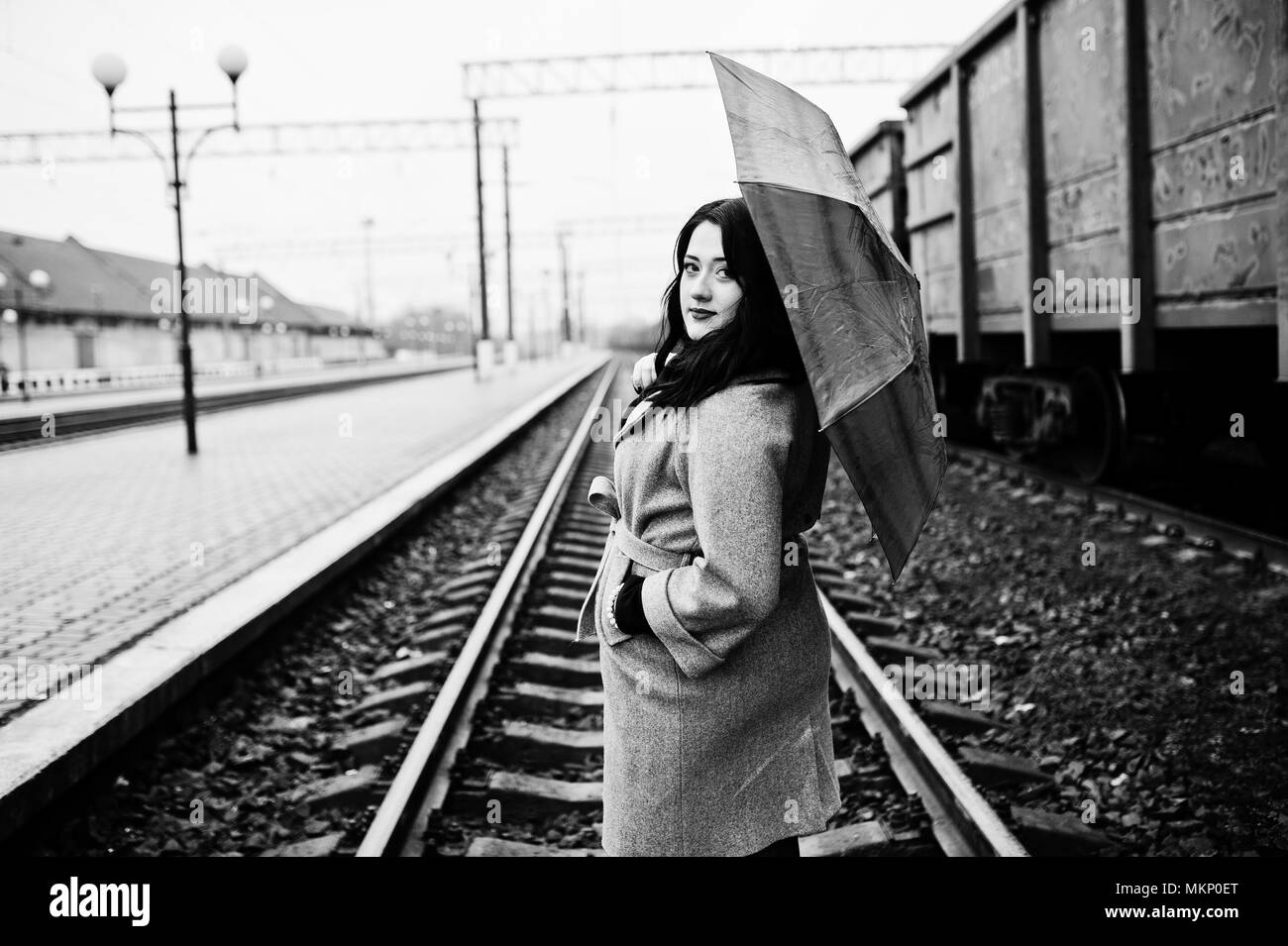 Brunette Mädchen im grauen Mantel mit roten Regenschirm im Bahnhof. Stockfoto