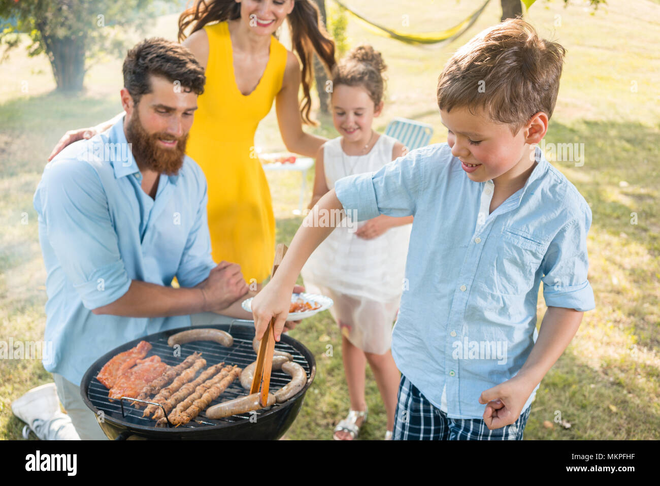 Vater und Sohn die Zubereitung von Fleisch auf Holzkohle Grill während Picknick Stockfoto